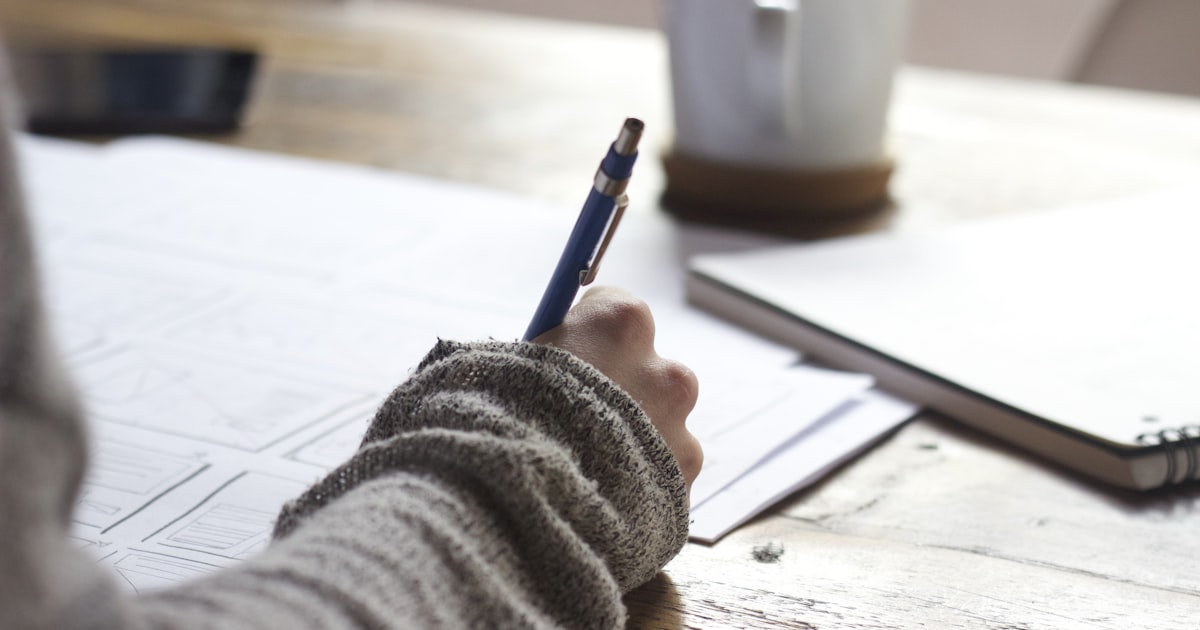 Person writing notes while doing research at a desk